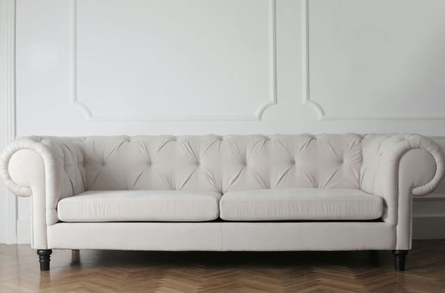 Cream-colored tufted couch against a white wall with molding, set on a hardwood floor.