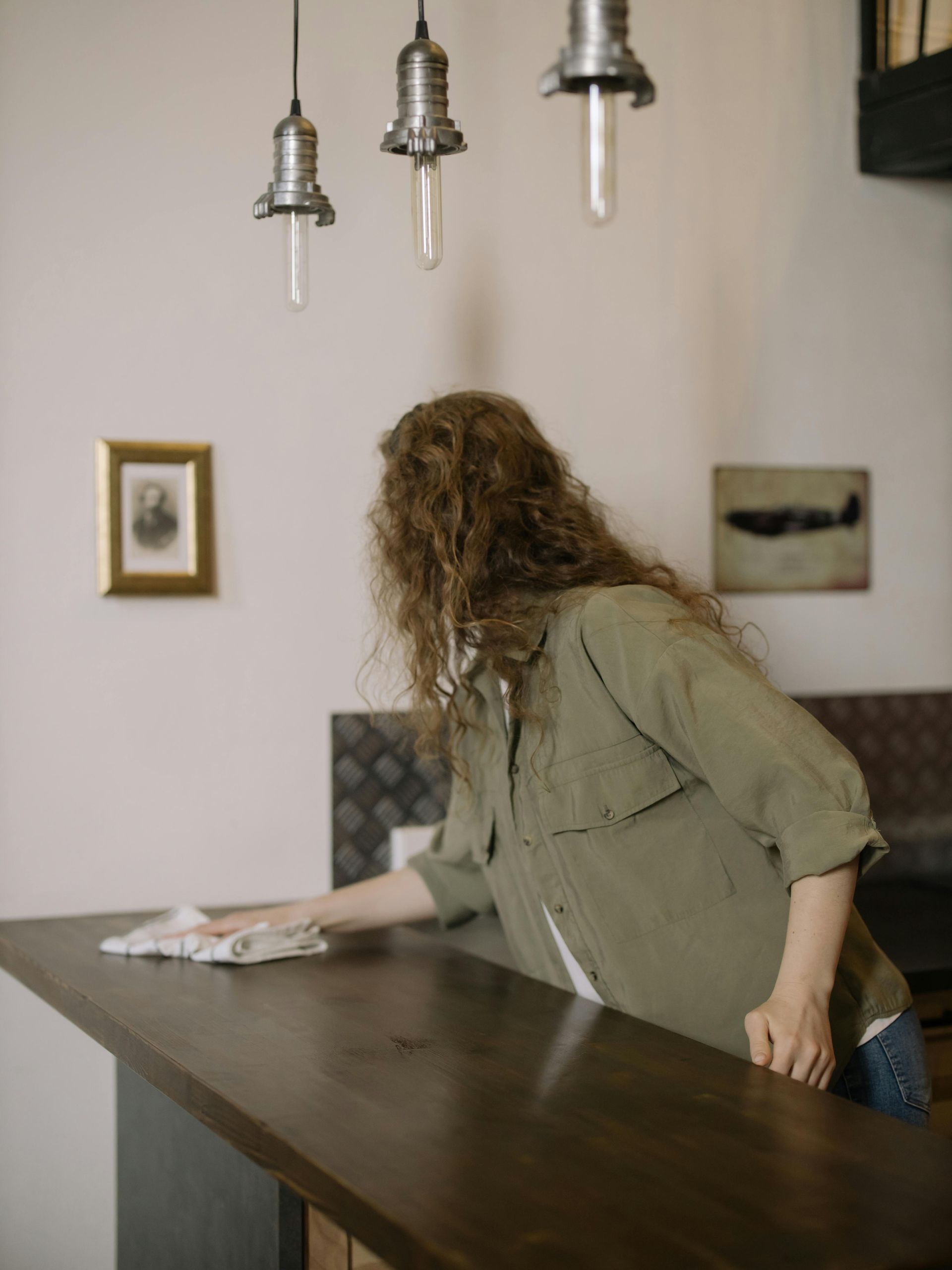 Woman wiping down a dark wooden counter under pendant lights.