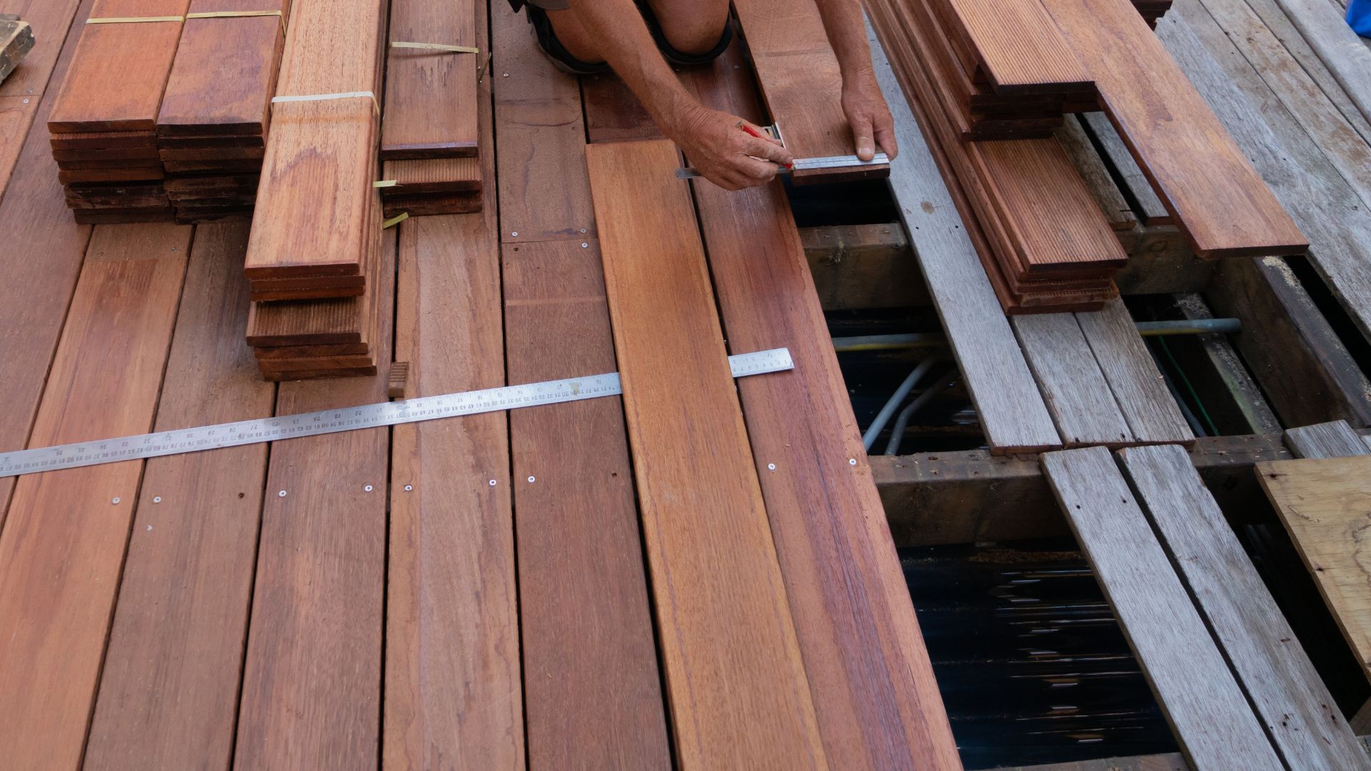 Worker measures and marks wooden planks on a deck under construction, showing detailed craftsmanship