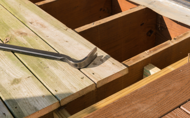 A photo of a deck that is getting it's old natural wood planks replaced with composite decking material. There is a crow bar laying on the deck.