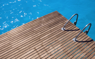 A photo of a deck sitting next to a pool. The deck has a ladder attached to it to enter into the pool.