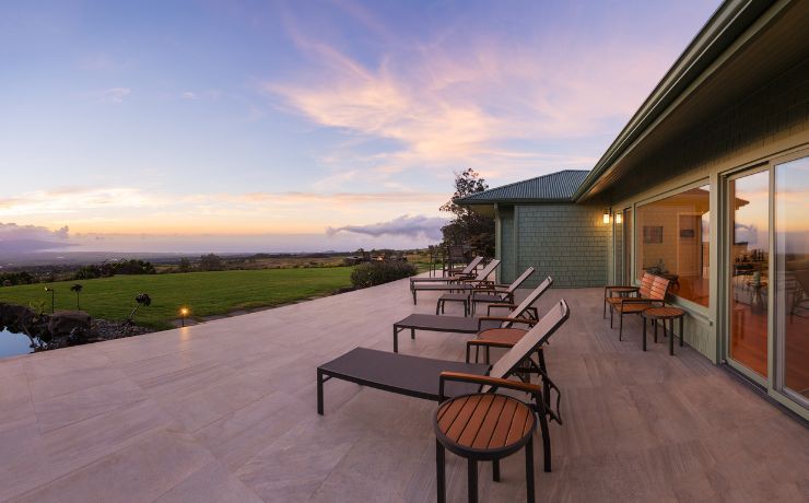 A photo of a beautiful and large deck in the backyard of a home in San Bernardino, California. The deck has 6 or 7 chairs and several tables. The deck is connected to the house, and you can enter the deck and house through a sliding glass door to the right of the photo.