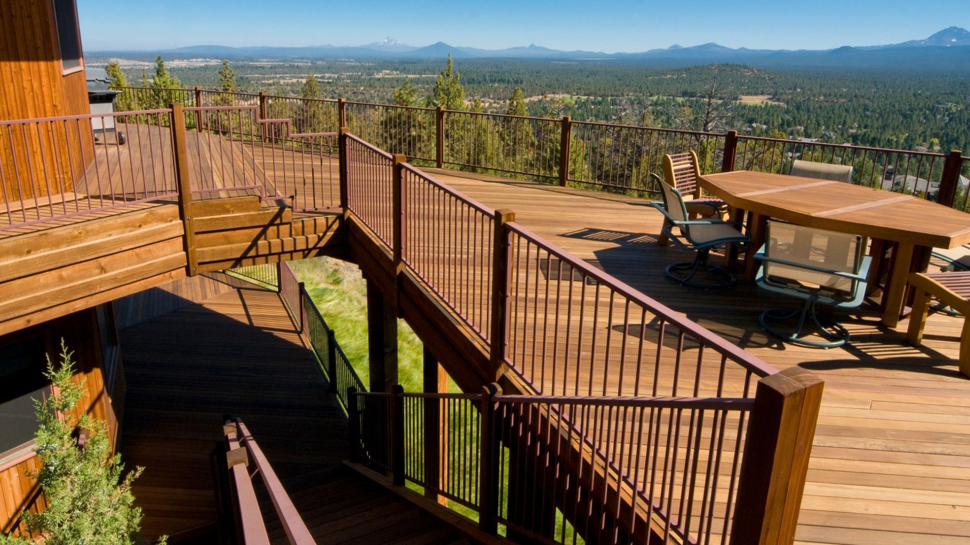 An expansive wooden deck in San Bernardino, CA, provides breathtaking panoramic views of the surrounding landscape. The multi-level deck features sturdy railings and ample space, perfect for outdoor activities and gatherings. In the foreground, a large wooden table with comfortable seating invites outdoor dining or relaxation. The stunning vista includes rolling hills, forests, and distant mountains, highlighting the natural beauty of San Bernardino. This deck exemplifies luxurious outdoor living in a scenic setting.