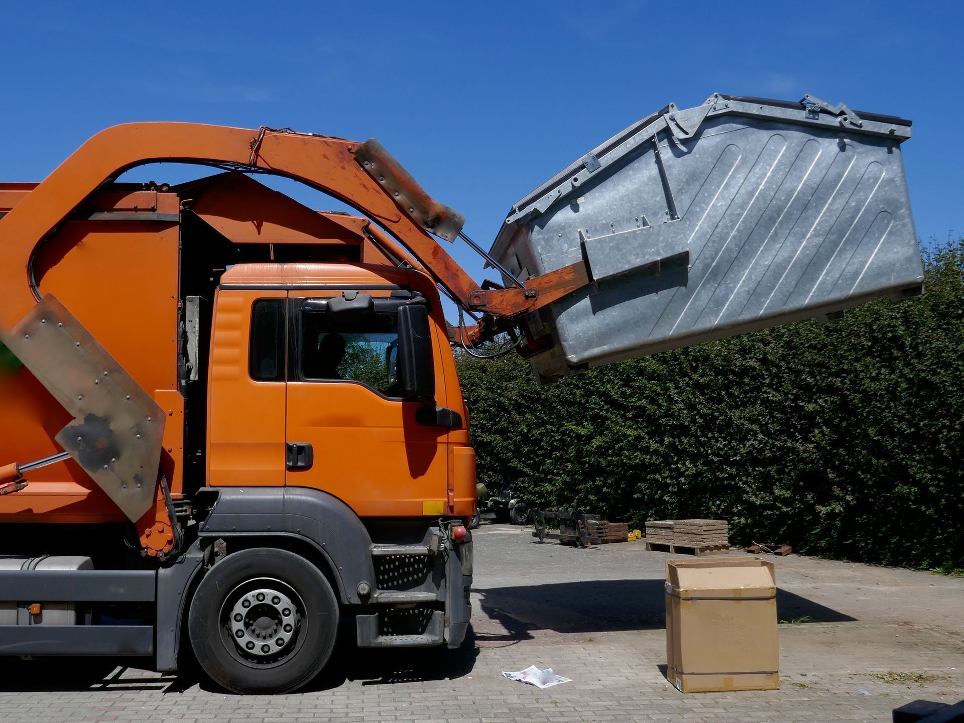 A garbage truck is loading a dumpster into the back of it.