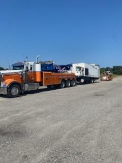 A tow truck is towing a semi truck down the road.