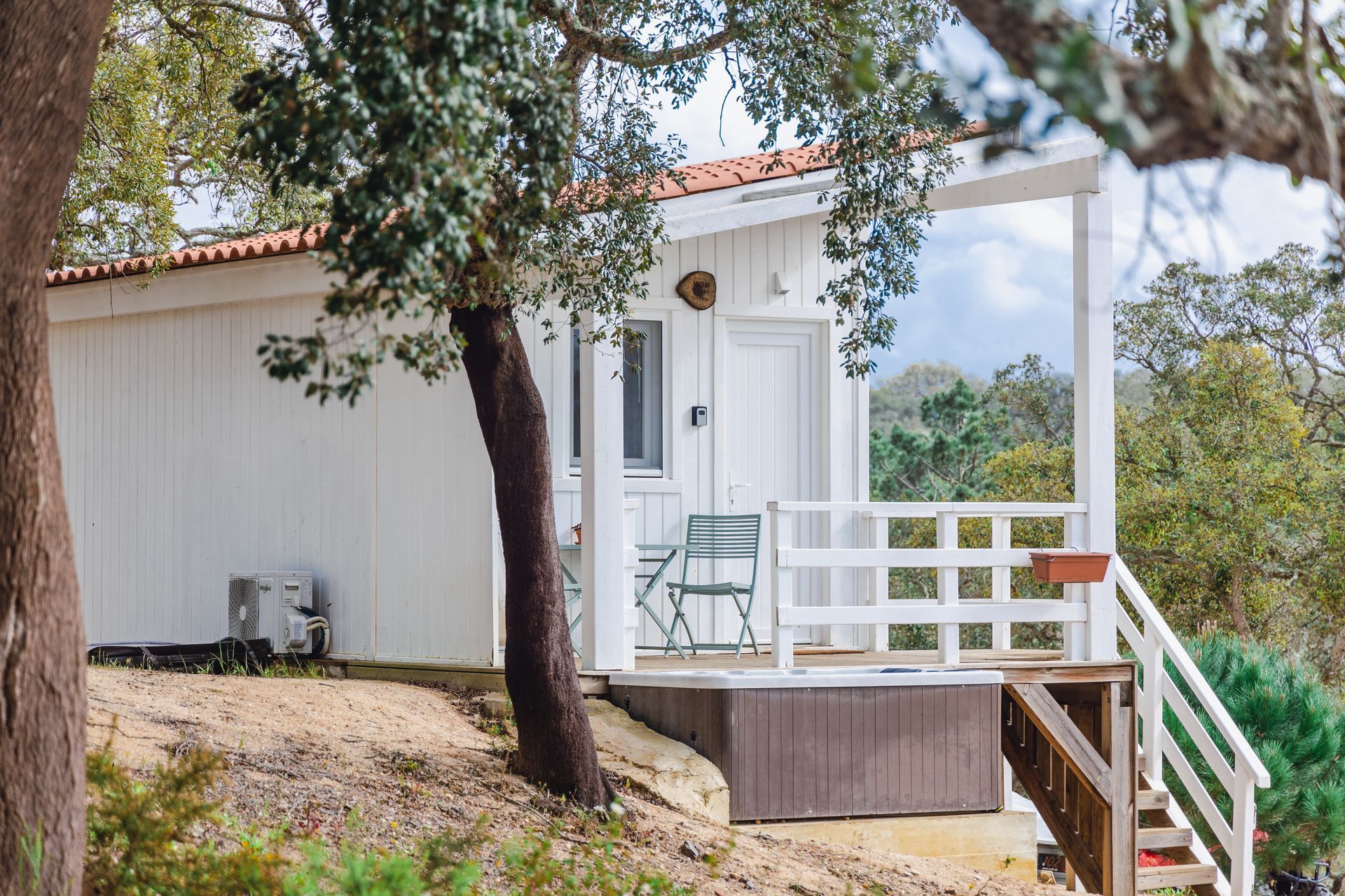 A small white house with a porch and stairs is surrounded by trees.