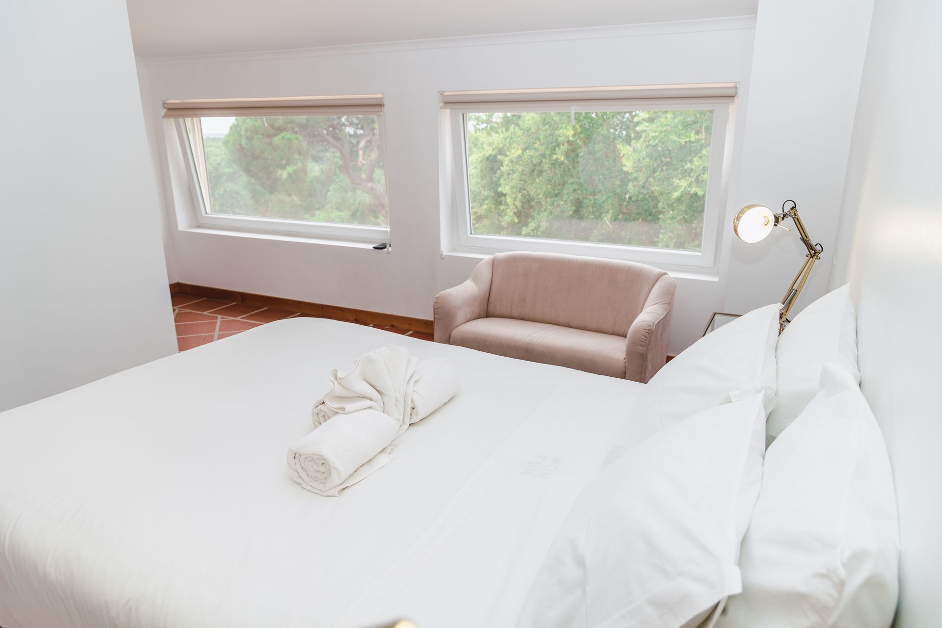 A bedroom with a bed , chair , lamp and two windows.