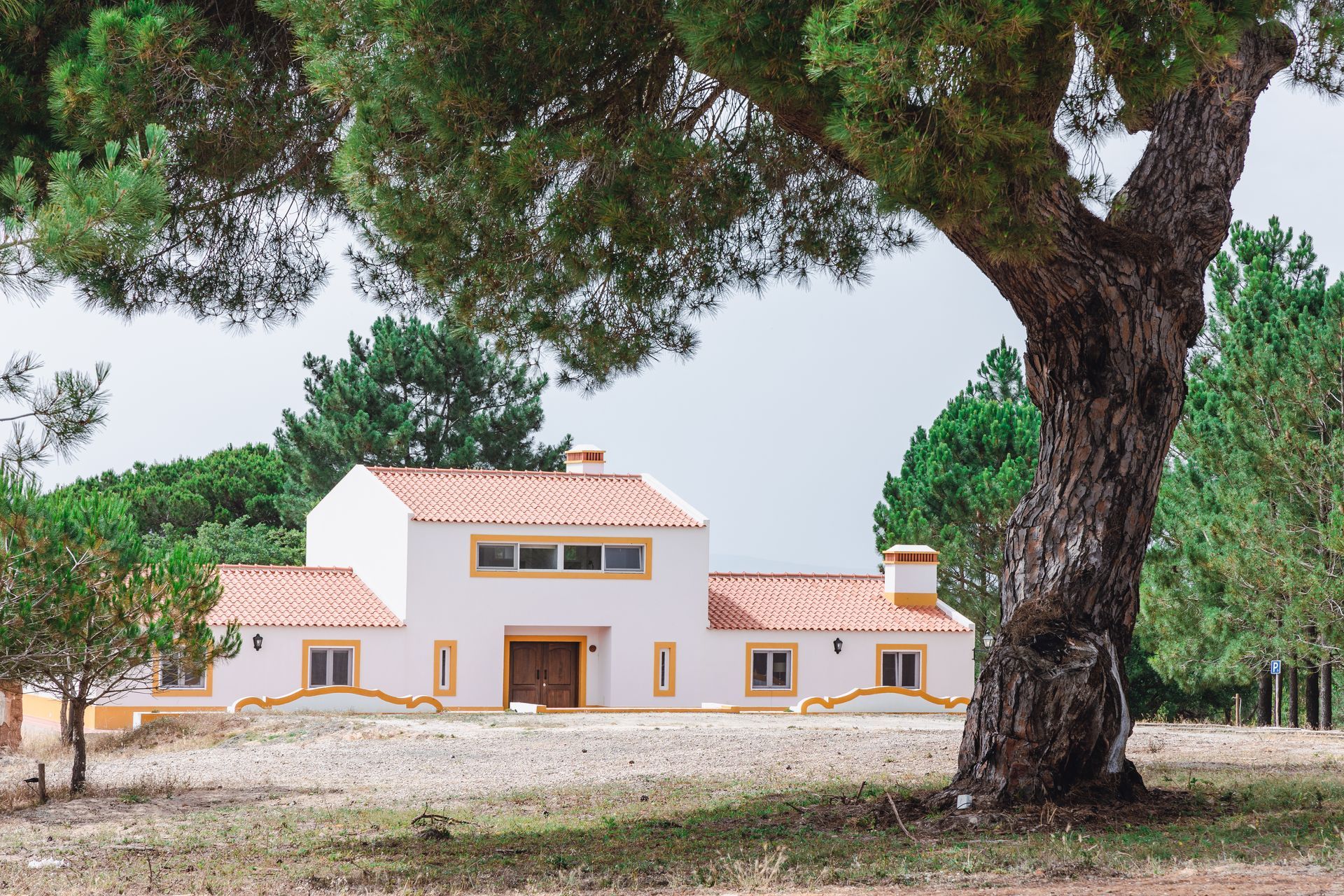 A white house with a red tile roof is surrounded by trees.
