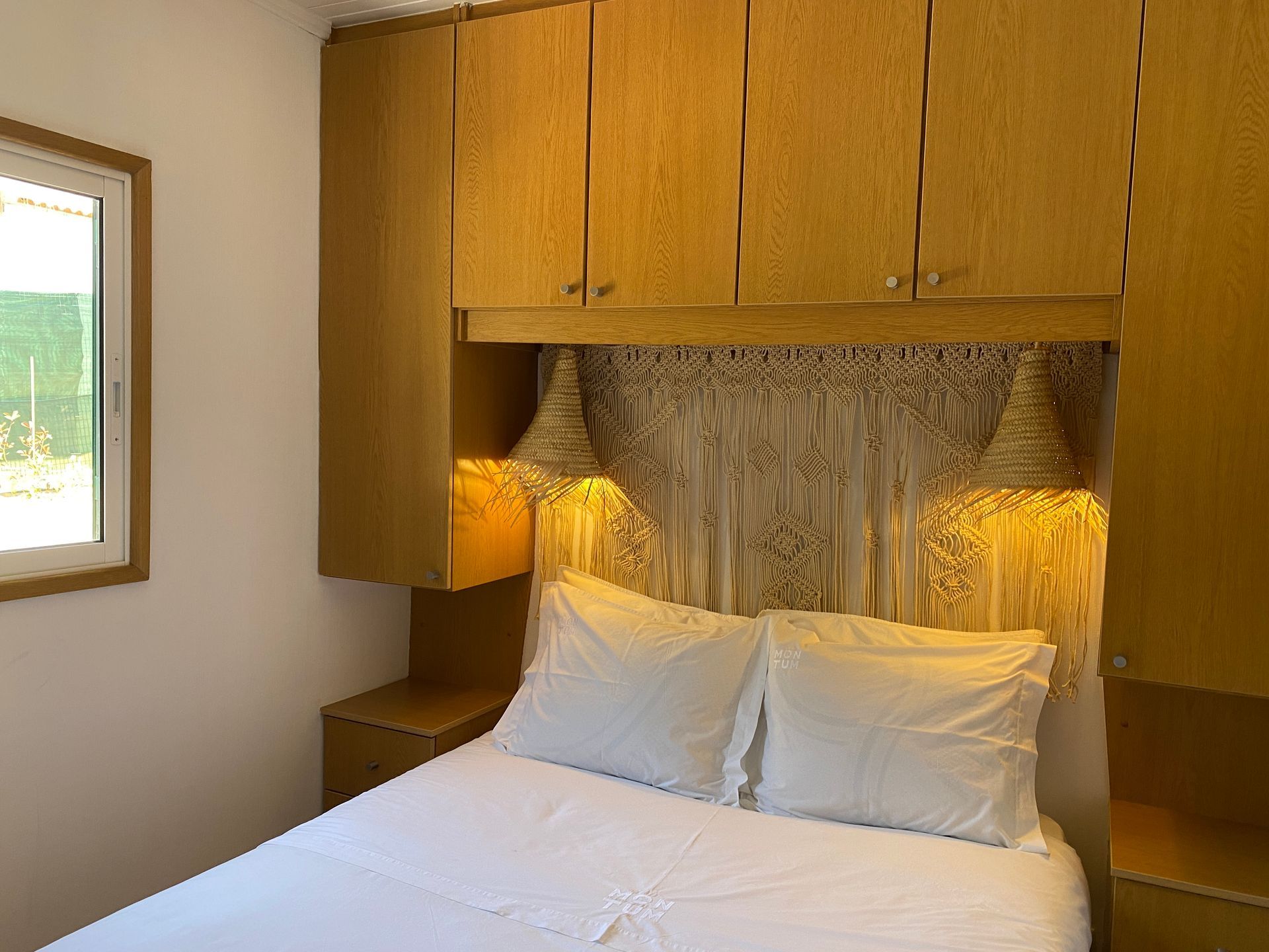 A bedroom with a bed , nightstand , cabinets and a window.