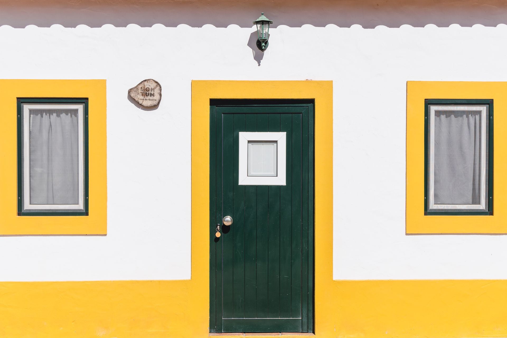 A yellow and white house with a green door and two windows.