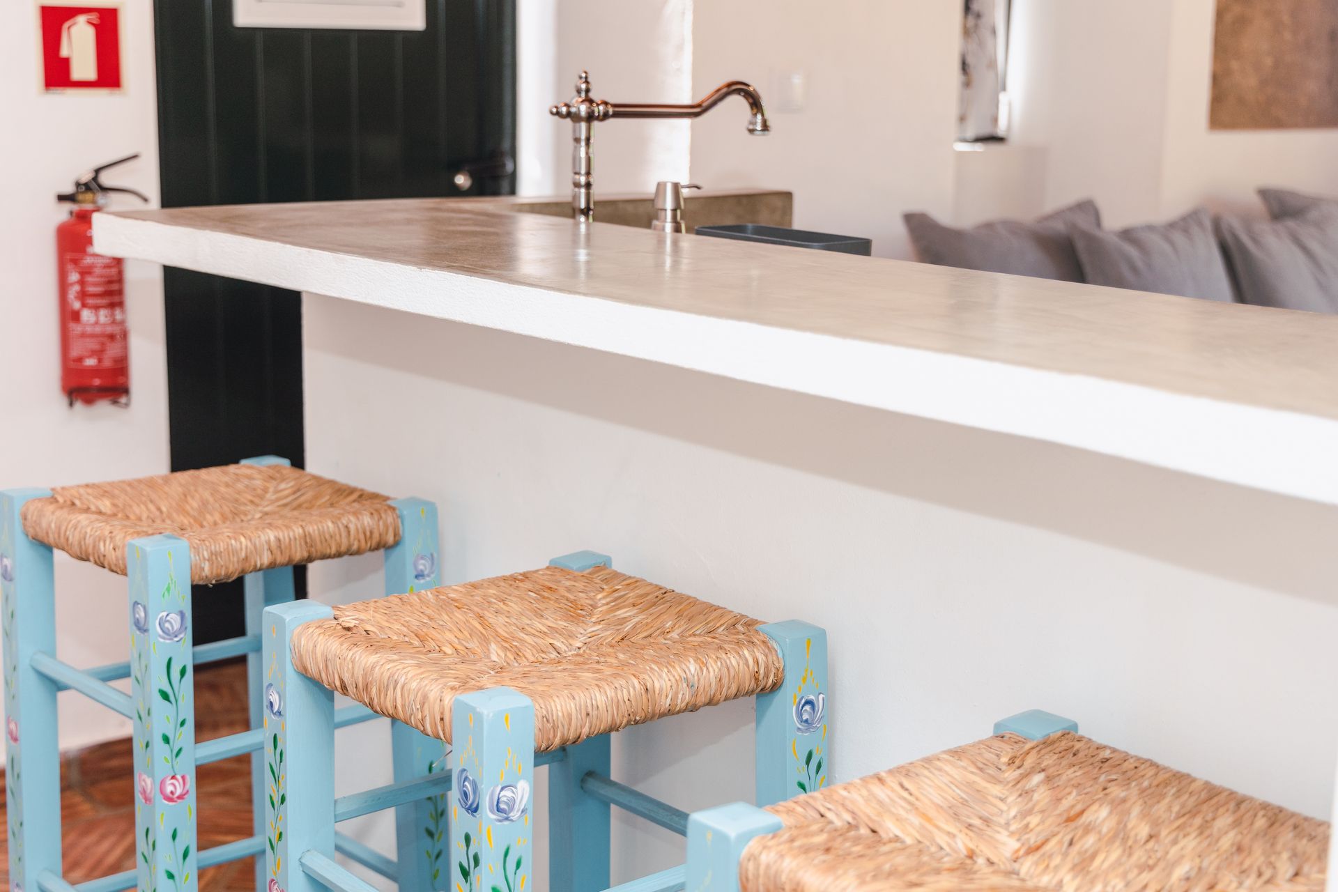 A kitchen counter with two wicker stools and a fire extinguisher.