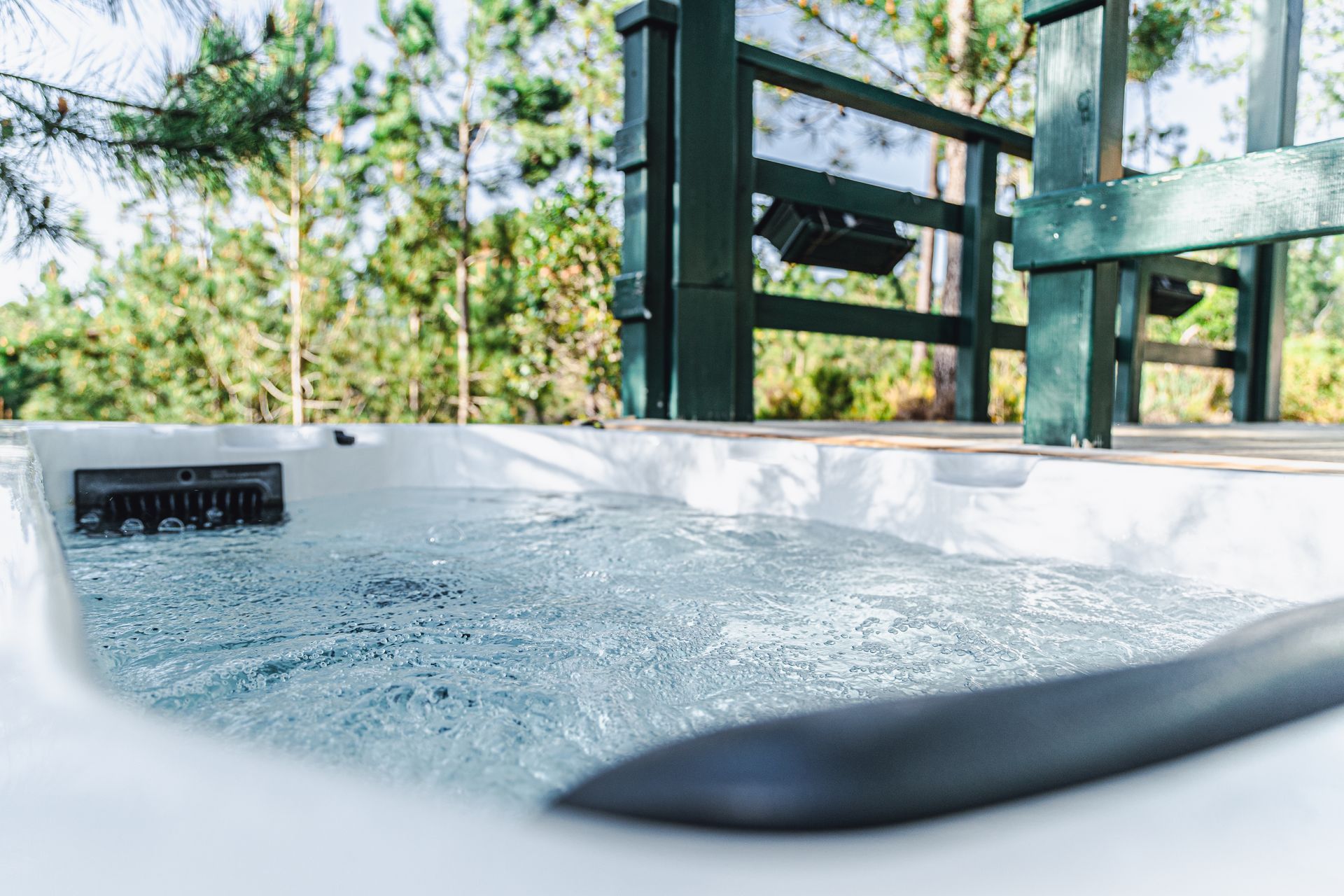 A hot tub is sitting on top of a wooden deck next to a fence.
