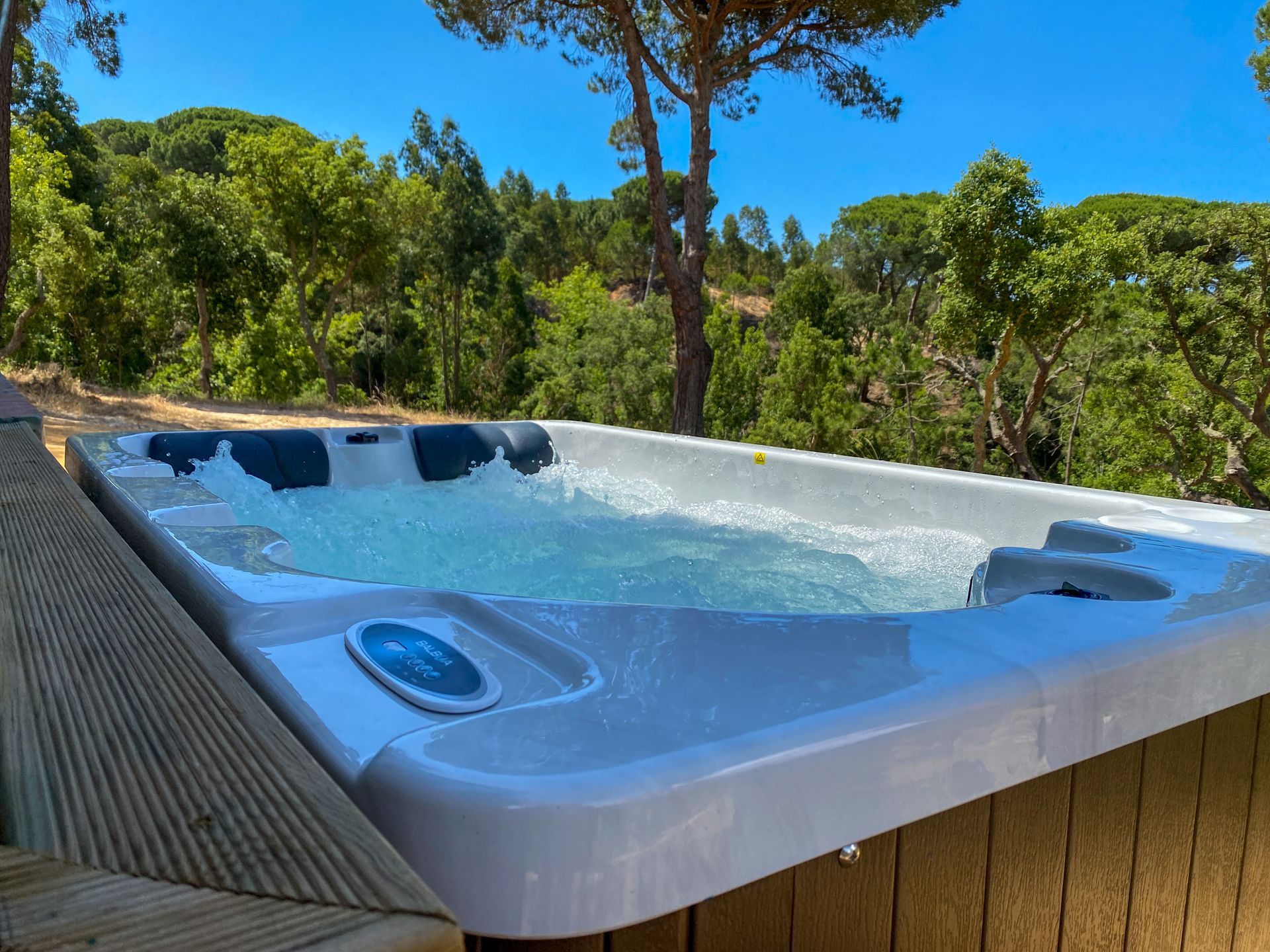 A hot tub is sitting on a wooden deck with trees in the background.