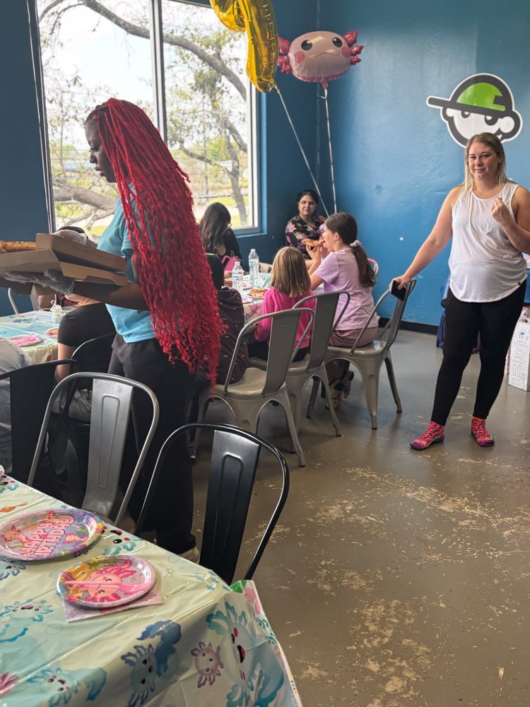 A woman with red hair is serving pizza to a group of children at a birthday party.
