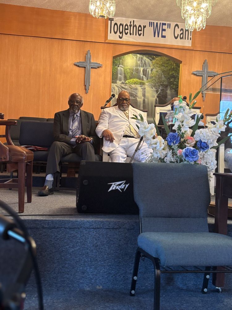 Two men are sitting on a stage in front of a sign that says together we can.