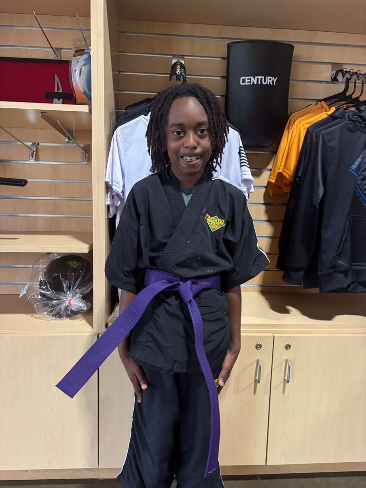 A young boy wearing a black karate uniform with a purple belt