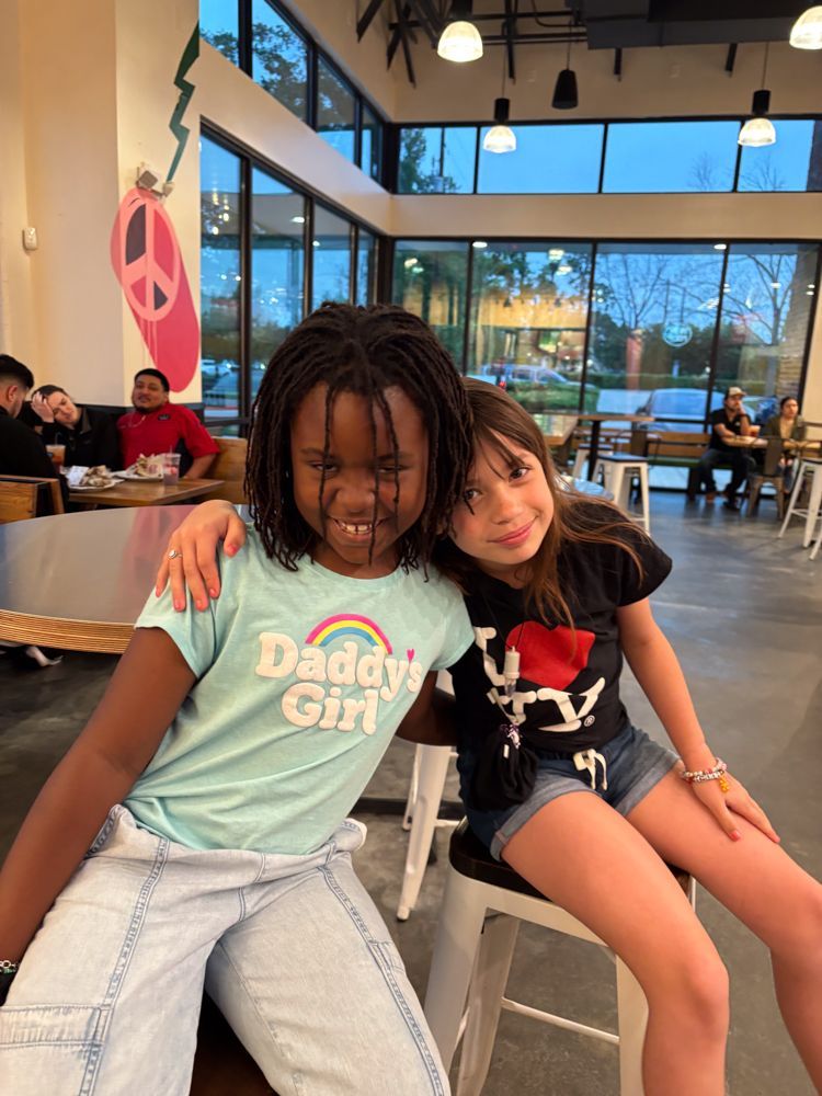 Two little girls are sitting next to each other in a restaurant.