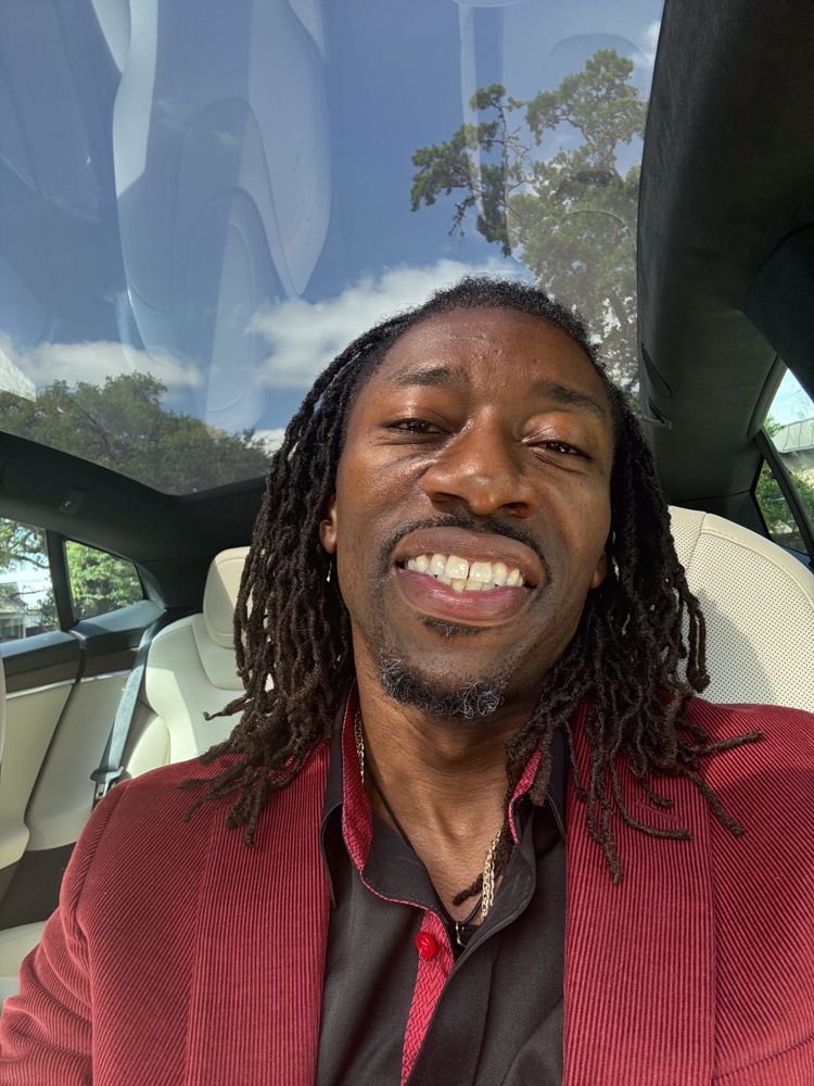 A man with dreadlocks is smiling while sitting in a car.