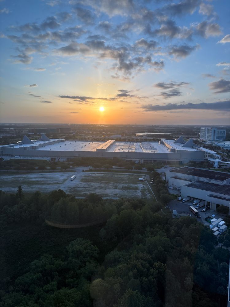 The sun is setting over a city with a lot of buildings and trees in the foreground.