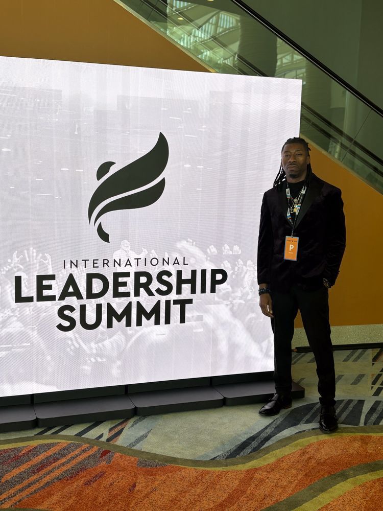 A man is standing in front of a large screen that says international leadership summit.