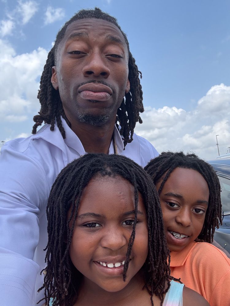 A man with dreadlocks is taking a selfie with two children.