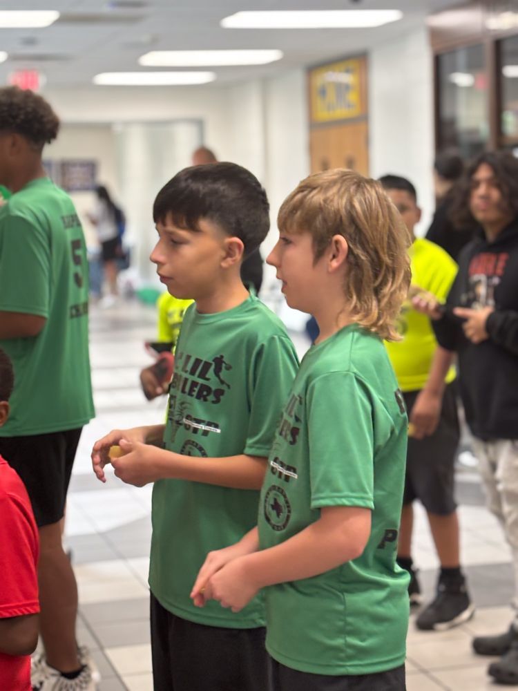 Two boys in green shirts are standing next to each other in a hallway.