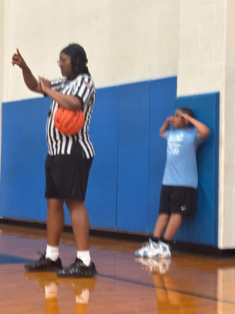 A referee holds a basketball while a boy leans against a wall