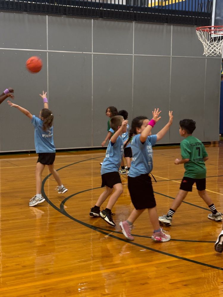 A group of children are playing basketball in a gym and one of them has the number 7 on his shirt