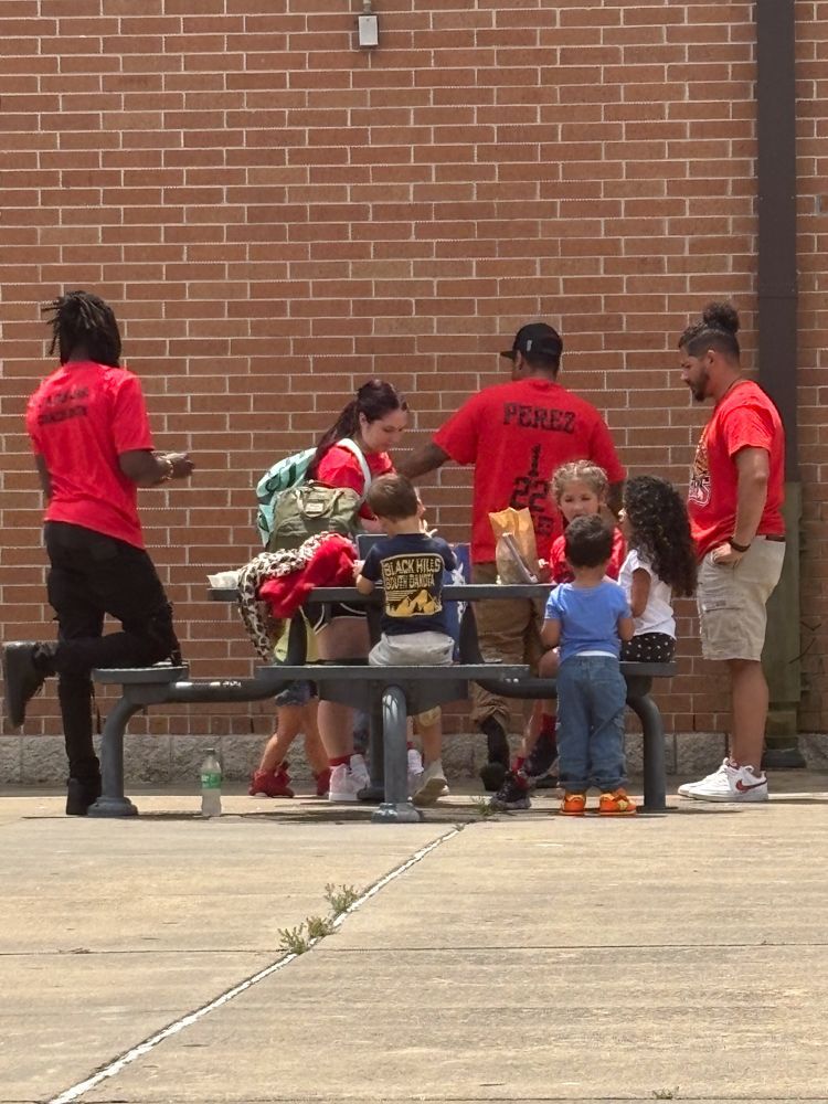 A group of people are sitting at a picnic table in front of a brick wall.