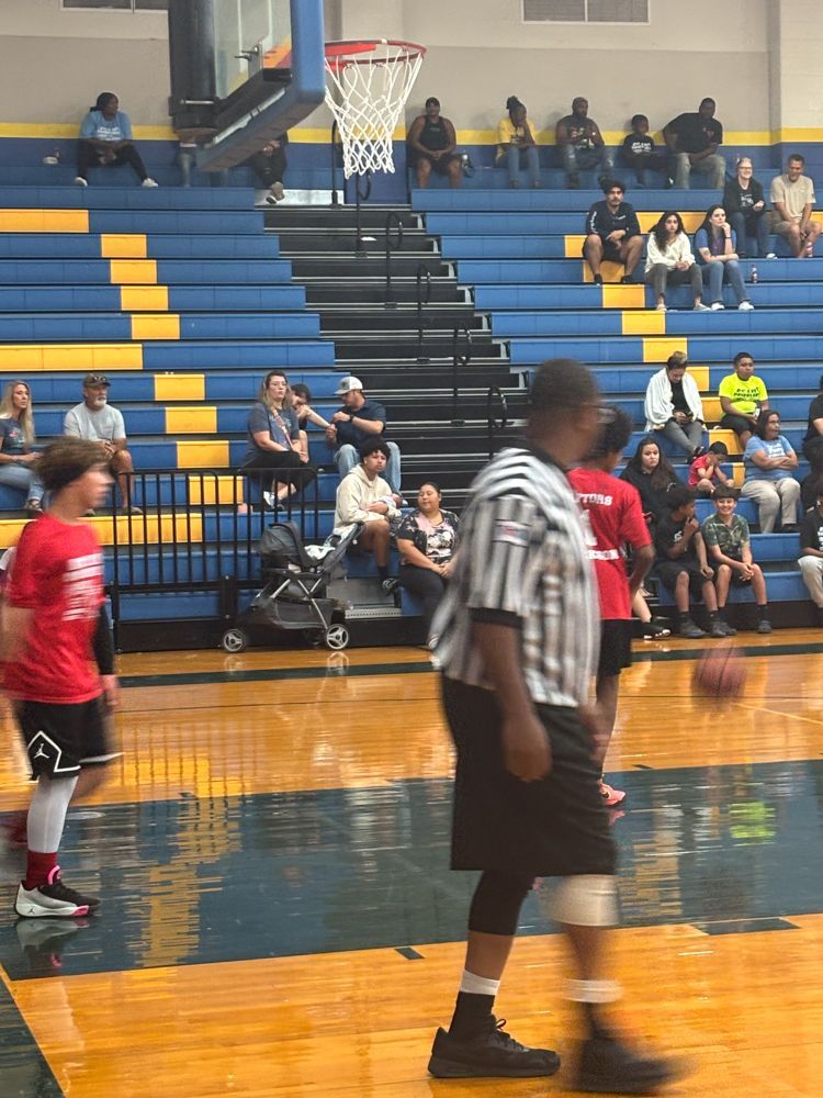 A referee is walking on a basketball court in front of a crowd.