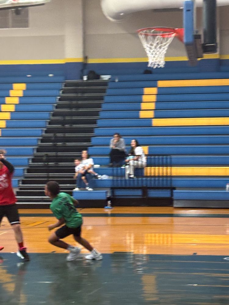A group of people are playing basketball in a gym with bleachers in the background