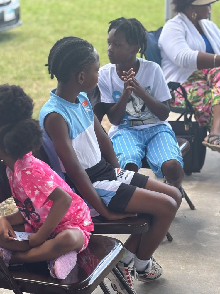 A group of people are sitting in folding chairs outside