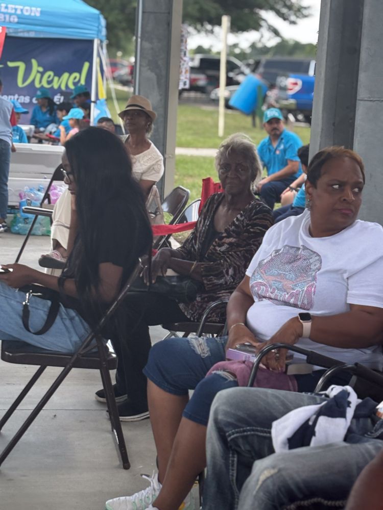 A group of people are sitting in chairs in front of a blue tent that says vicmel