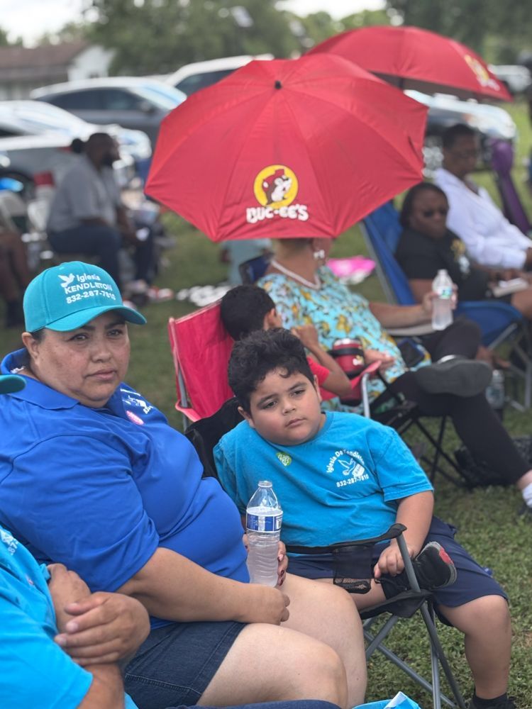A group of people are sitting in the grass under umbrellas.