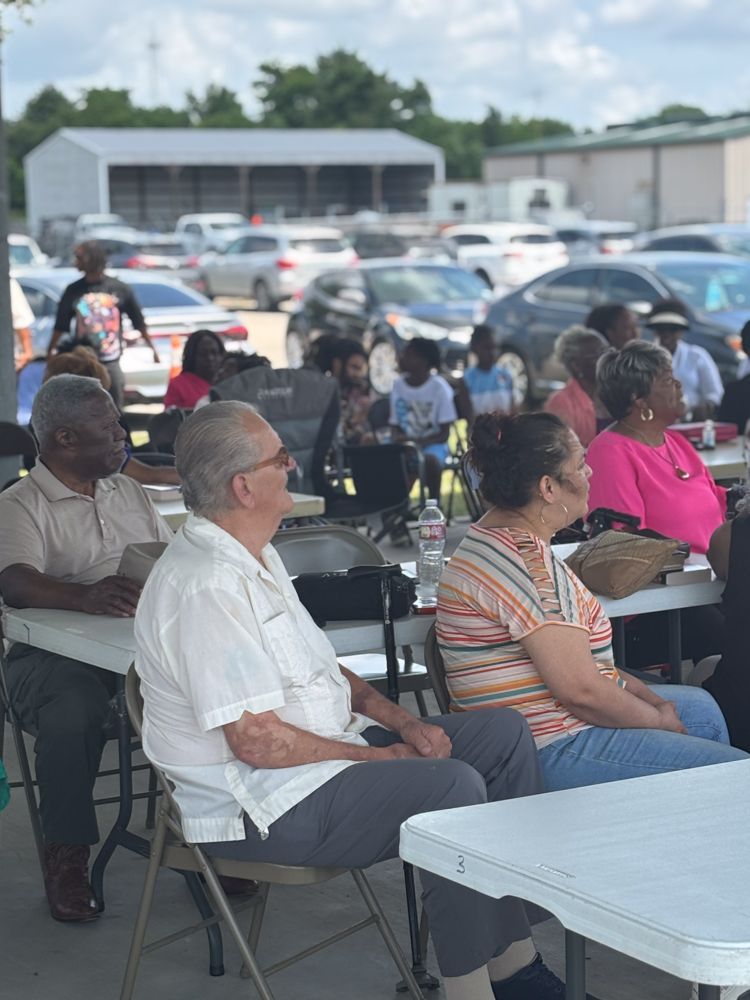 A group of people are sitting at tables in a parking lot.