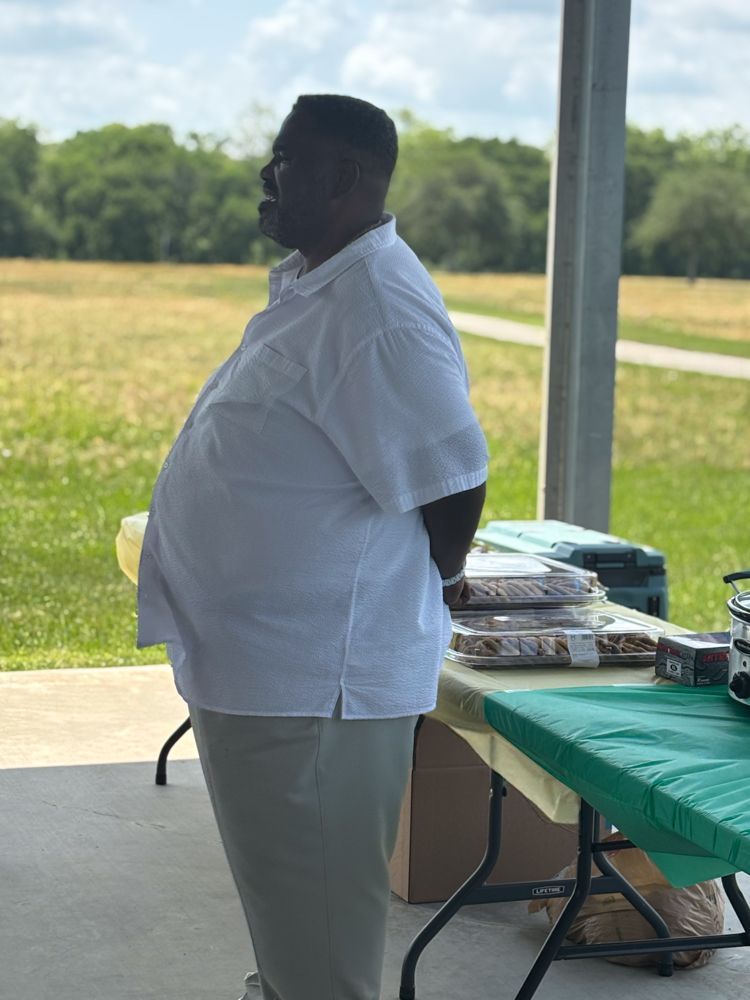 A man in a white shirt is standing in front of a table.