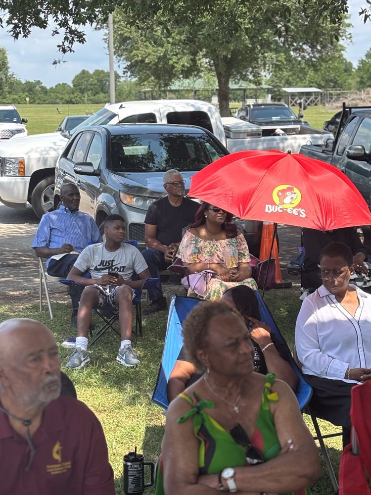 A group of people are sitting under an umbrella in a park.
