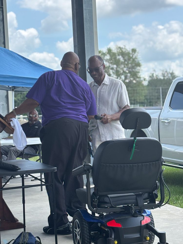 A man in a purple shirt is standing next to a man in a mobility scooter.