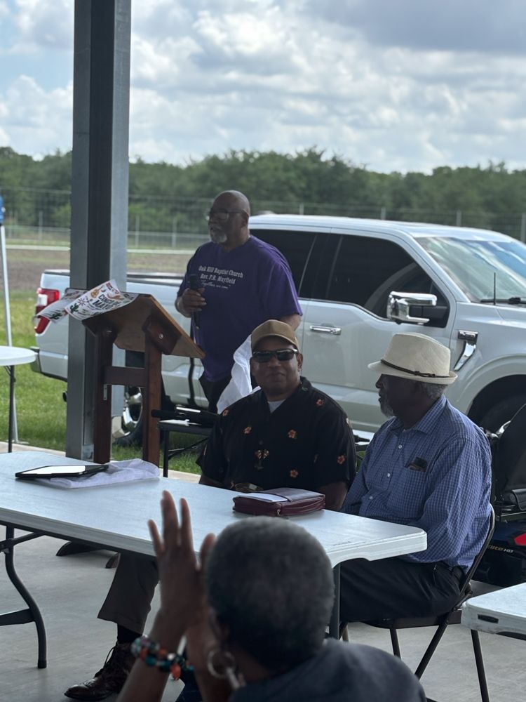 A man in a purple shirt is giving a speech to a group of men