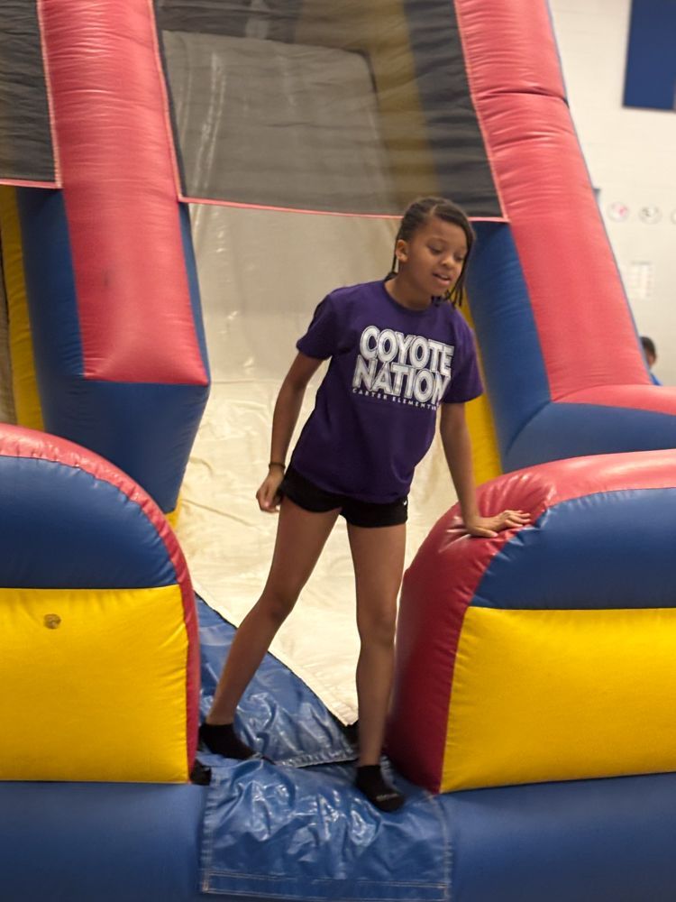 A girl in a purple coyote nation shirt is standing on a bouncy house.