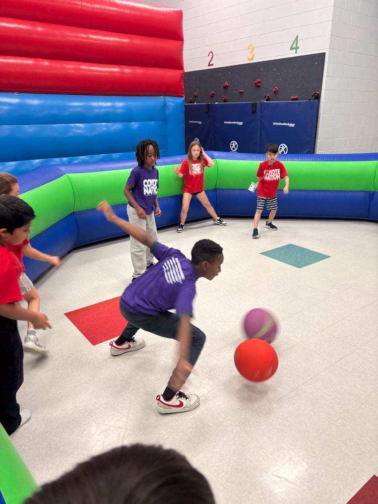A group of children are playing a game of dodgeball in a gym.