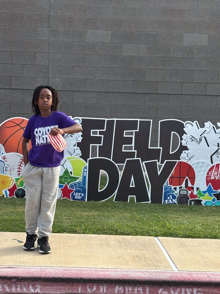 A young boy is standing in front of a sign that says field day