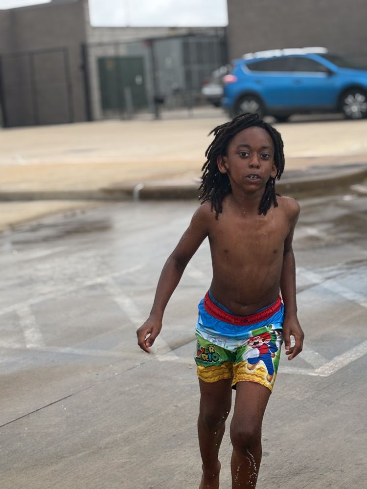 A young boy without a shirt is walking in the rain.