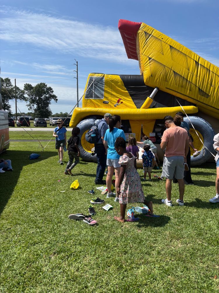 A group of people are standing in a grassy field in front of an inflatable slide.