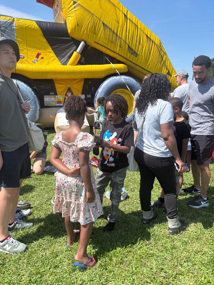 A group of people are standing in the grass in front of an inflatable slide.