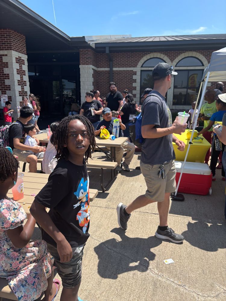 A boy wearing a sonic the hedgehog shirt is standing in front of a crowd of people.