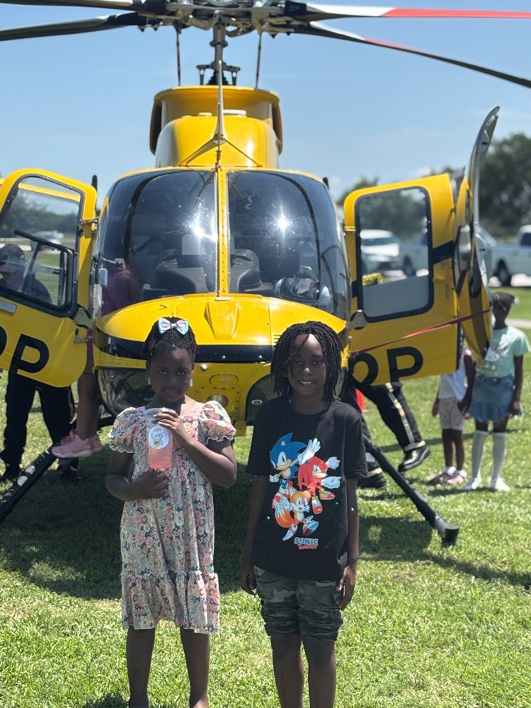 Two children are standing in front of a yellow helicopter that says rp on the side