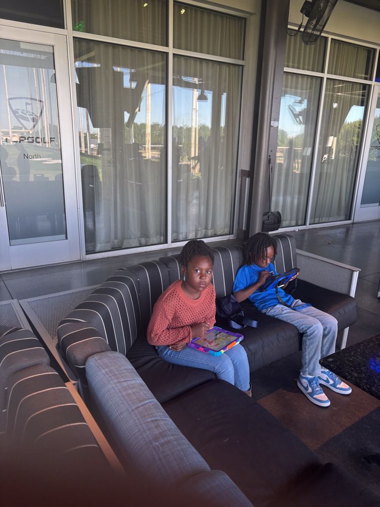 Two children are sitting on a couch looking at their tablets.