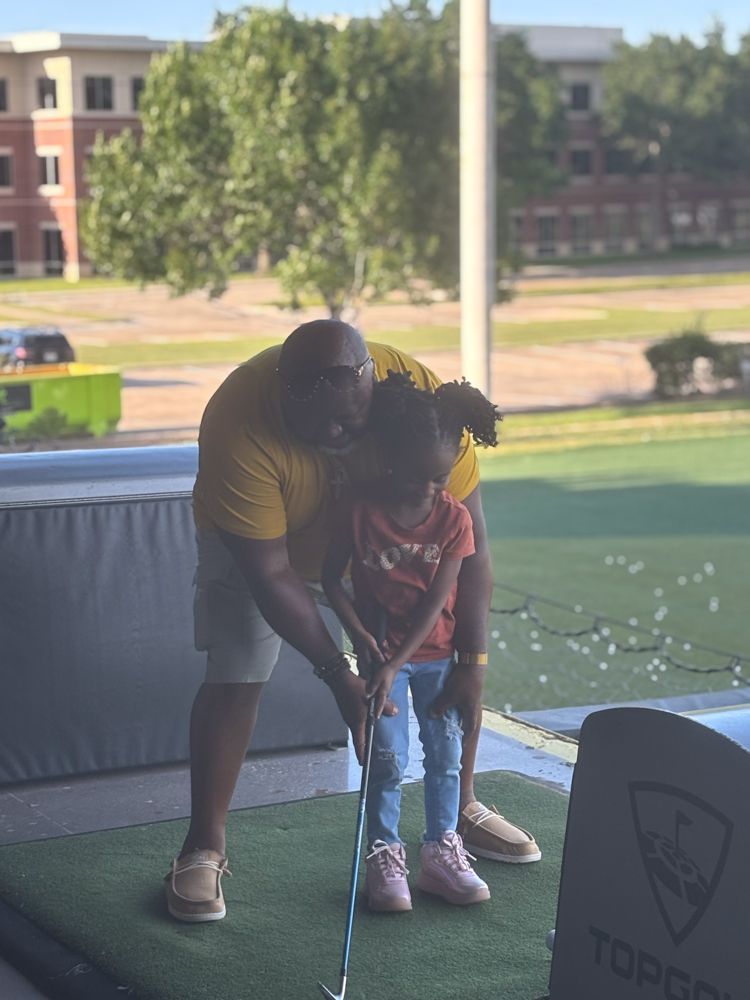 A man is teaching a little girl how to play golf