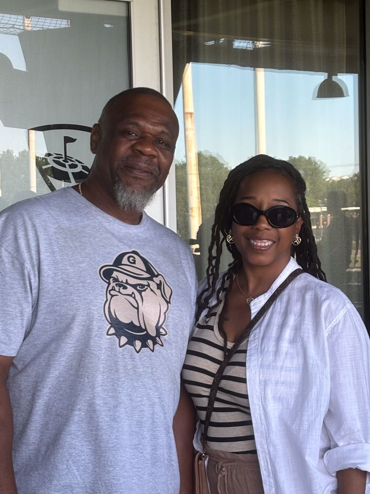A man and a woman are posing for a picture in front of a window.